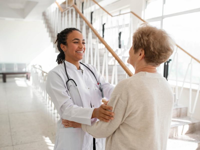 Médica sorridente acolhendo paciente idosa no hospital, representando um retorno de consulta com cuidado e empatia.
