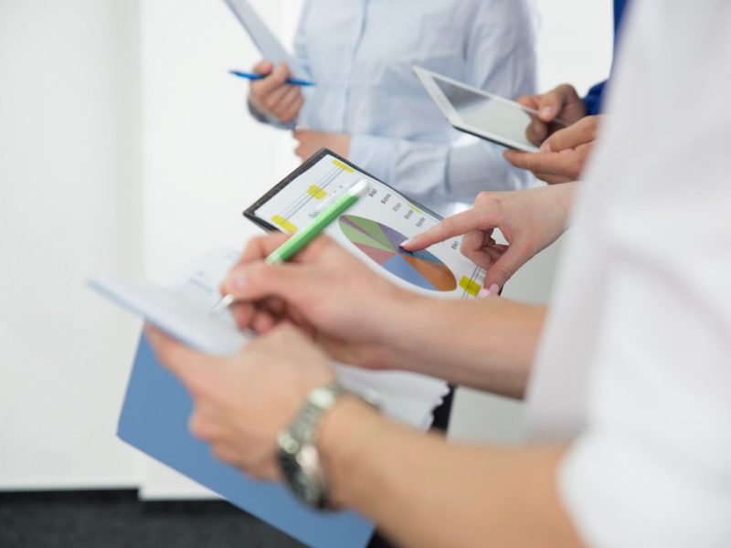 Mãos segurando caderno, tablet e anotando informações de pacientes e riscos ocupacionais.