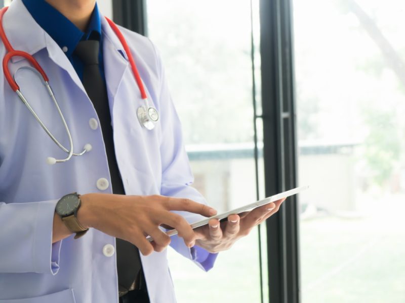 Médico com estetoscópio usando tablet, representando um sistema de saúde digital.
