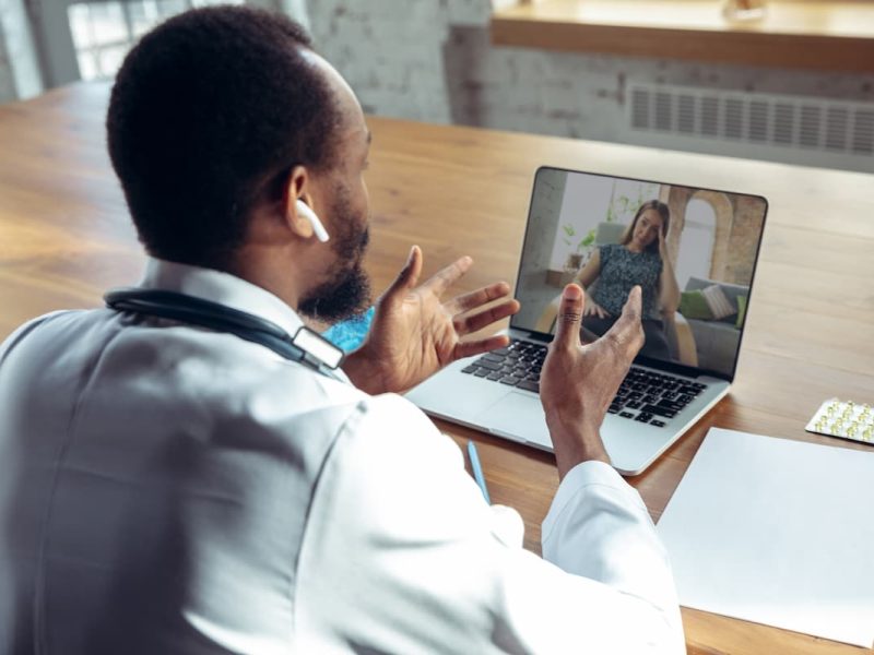 Médico realiza telediagnóstico em consulta online, conversando com paciente por videochamada em um ambiente iluminado.