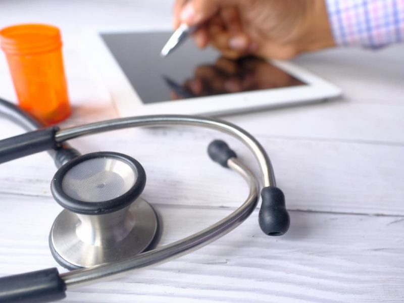 Médico usando tablet com calculadora ao lado, simbolizando os tipos de tributação em estabelecimentos médicos.