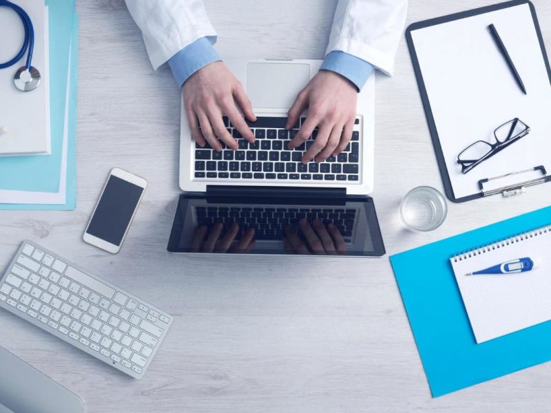 Itens tecnológicos como laptop, celular e teclado, simbolizando a transformação digital na clínica ou consultório médico.