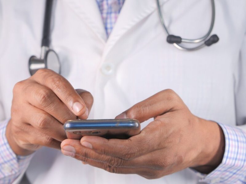 Um médico de jaleco branco e estetoscópio utiliza o celular para gerenciar a comunicação da clínica com o whatsapp business.